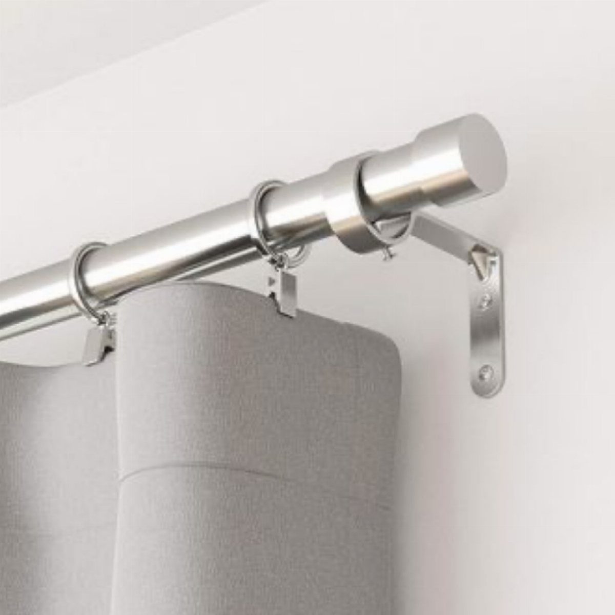 Silver metal curtain rod with grey curtains mounted on a white wall