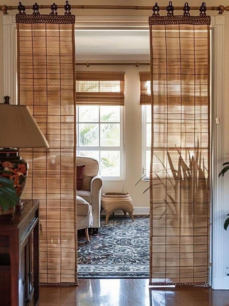 Brown woven bamboo shades hanging in a doorway of a bright living room.