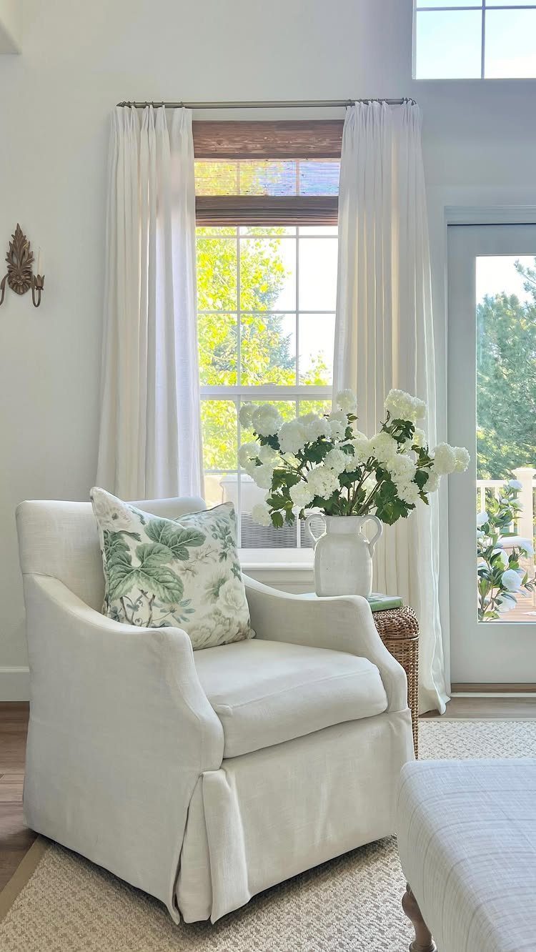 White curtains framing a window in a bright living room with a white armchair.