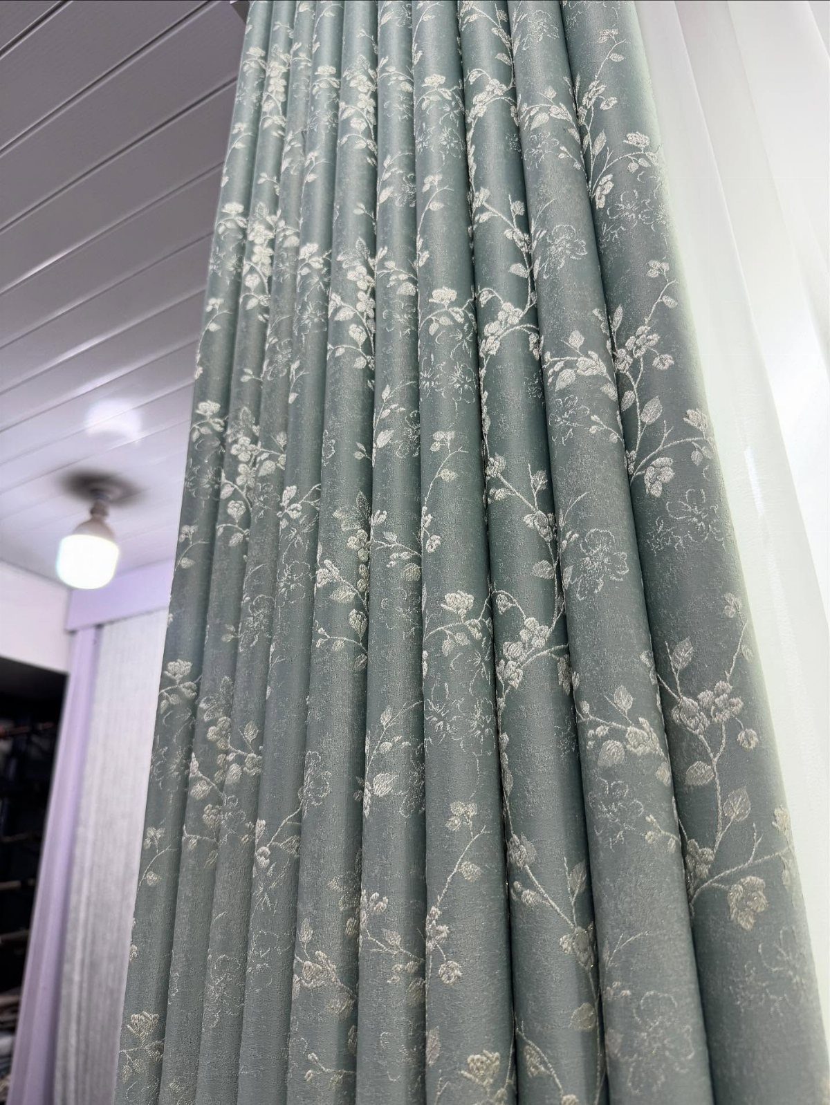 Light blue-grey curtains featuring a delicate white floral pattern hanging in folds.
