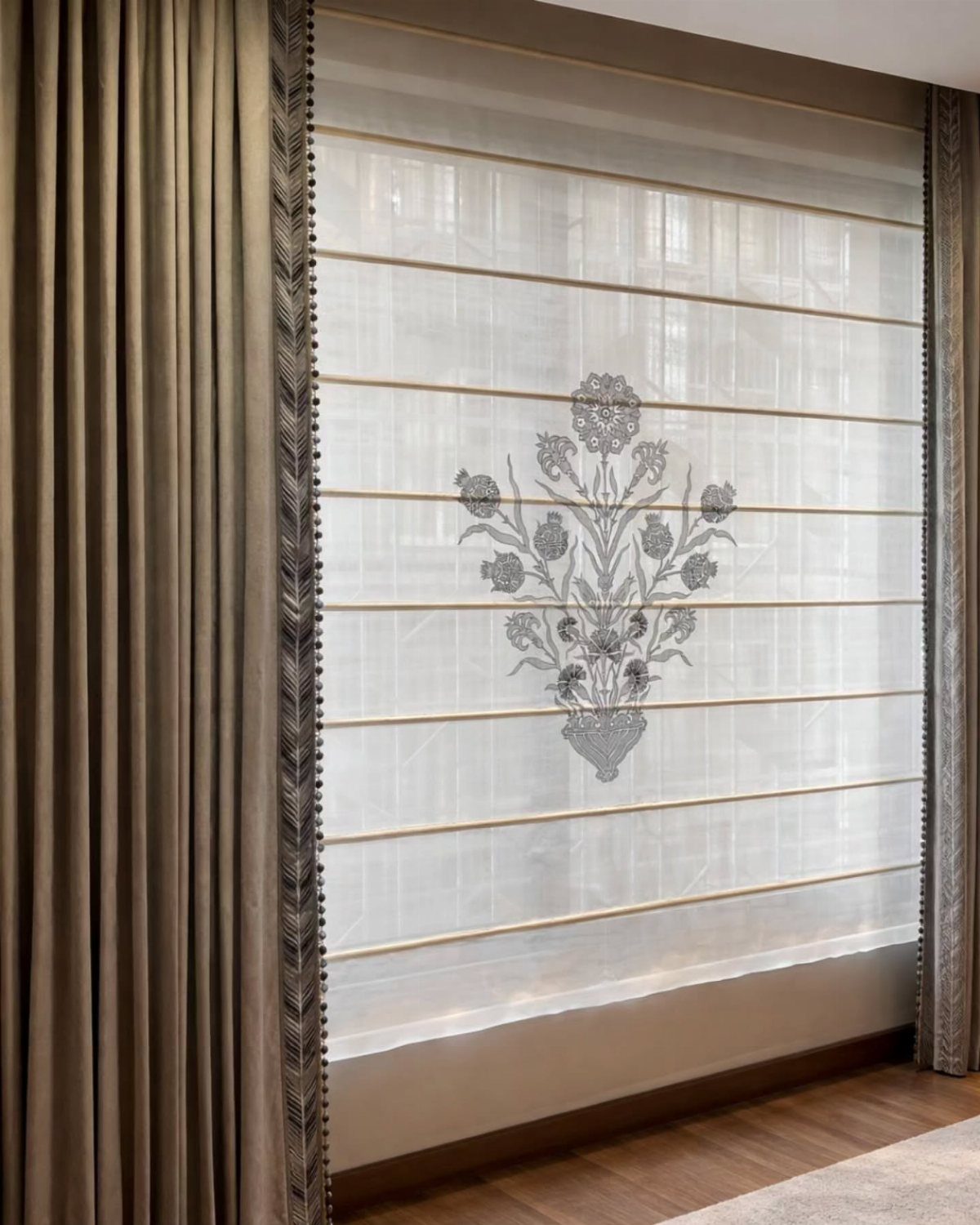 Beige opaque curtains framing a white semi-sheer Roman shade with floral embroidery.