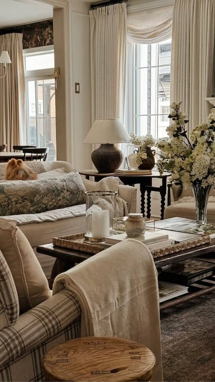 Cream curtains framing a window in a neutral living room with beige furniture.