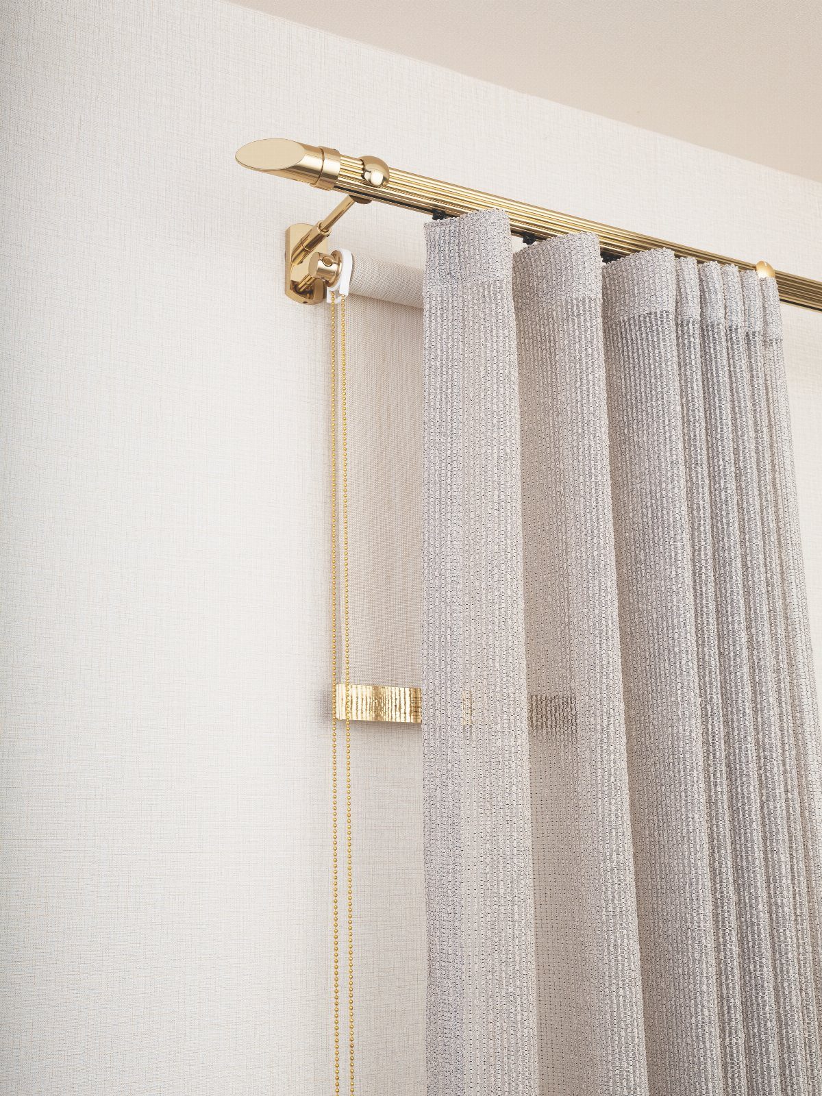 Gold curtain rod with decorative finial holding grey textured and sheer curtains.