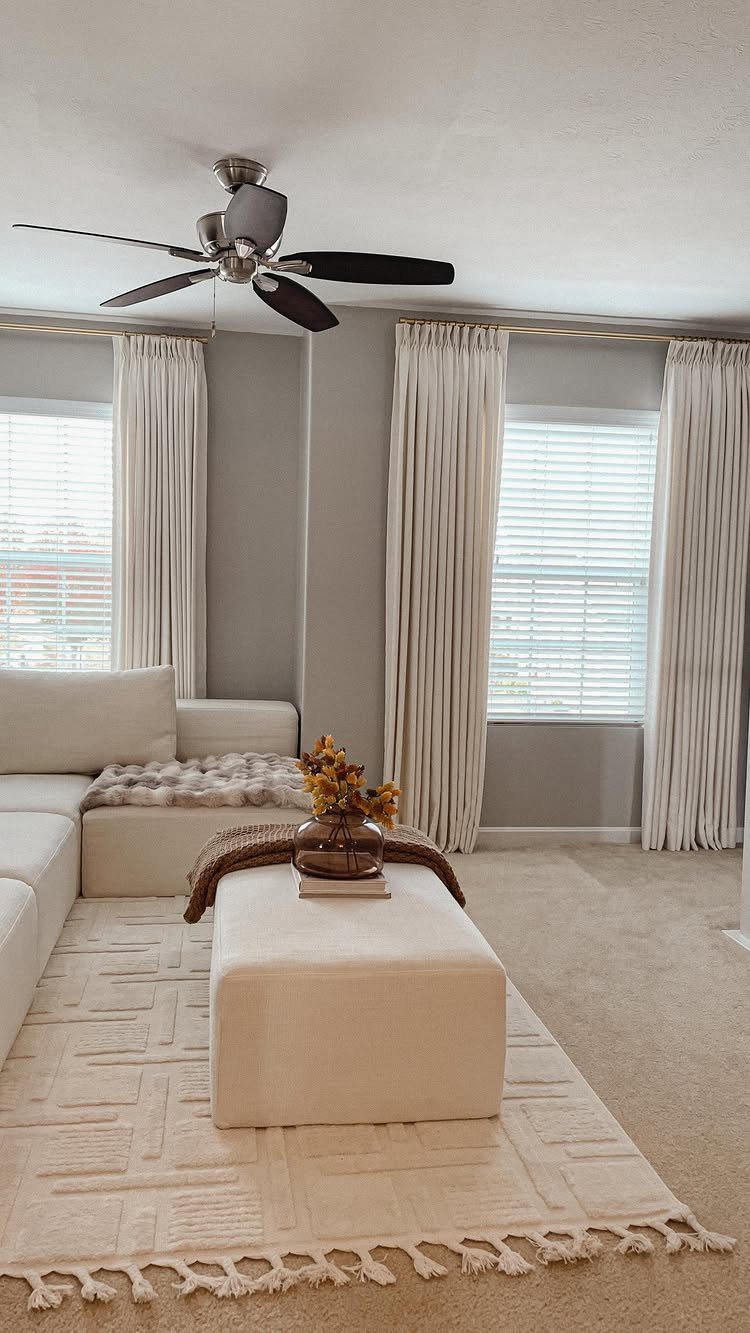 White curtains in a neutral living room with a white sofa and ottoman.