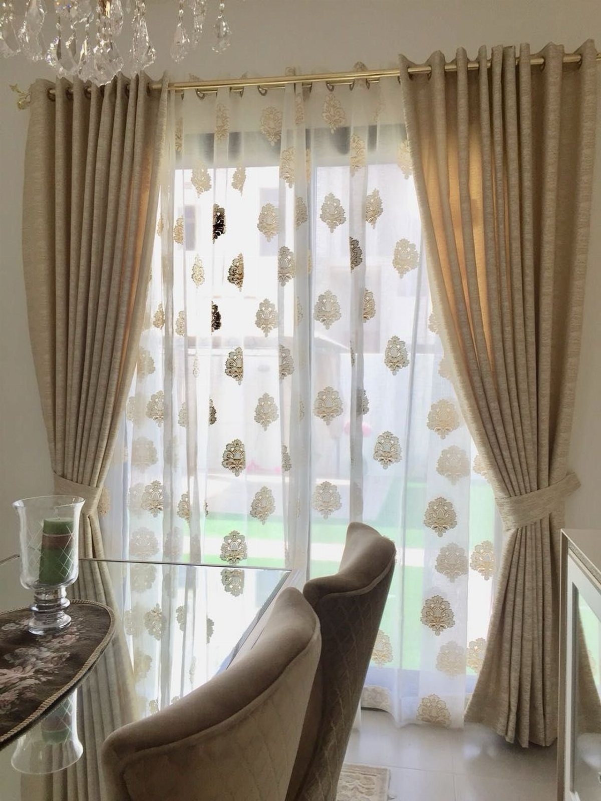 Beige heavy drapes layered with white and gold patterned sheer curtains.