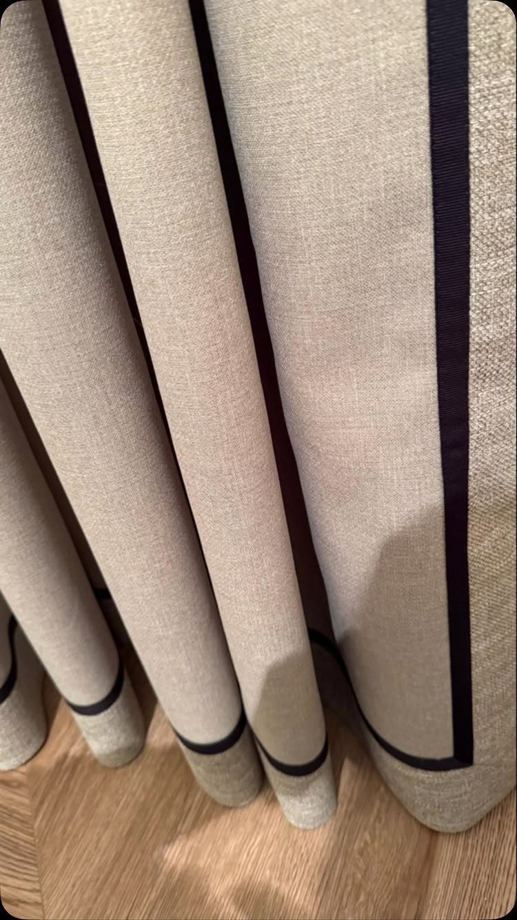 Beige textured curtains with dark navy blue borders hanging over wooden flooring.