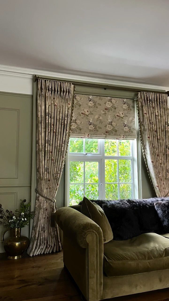 Floral patterned curtains and matching Roman shade in a living room with velvet sofa.