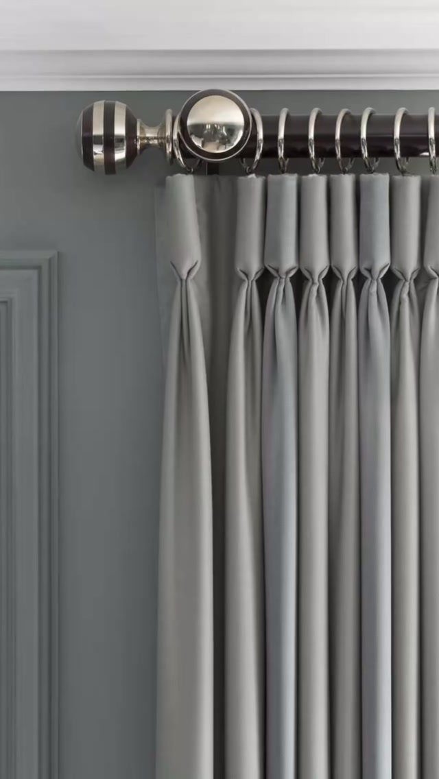 Grey pleated curtains on a dark rod with a decorative striped finial.