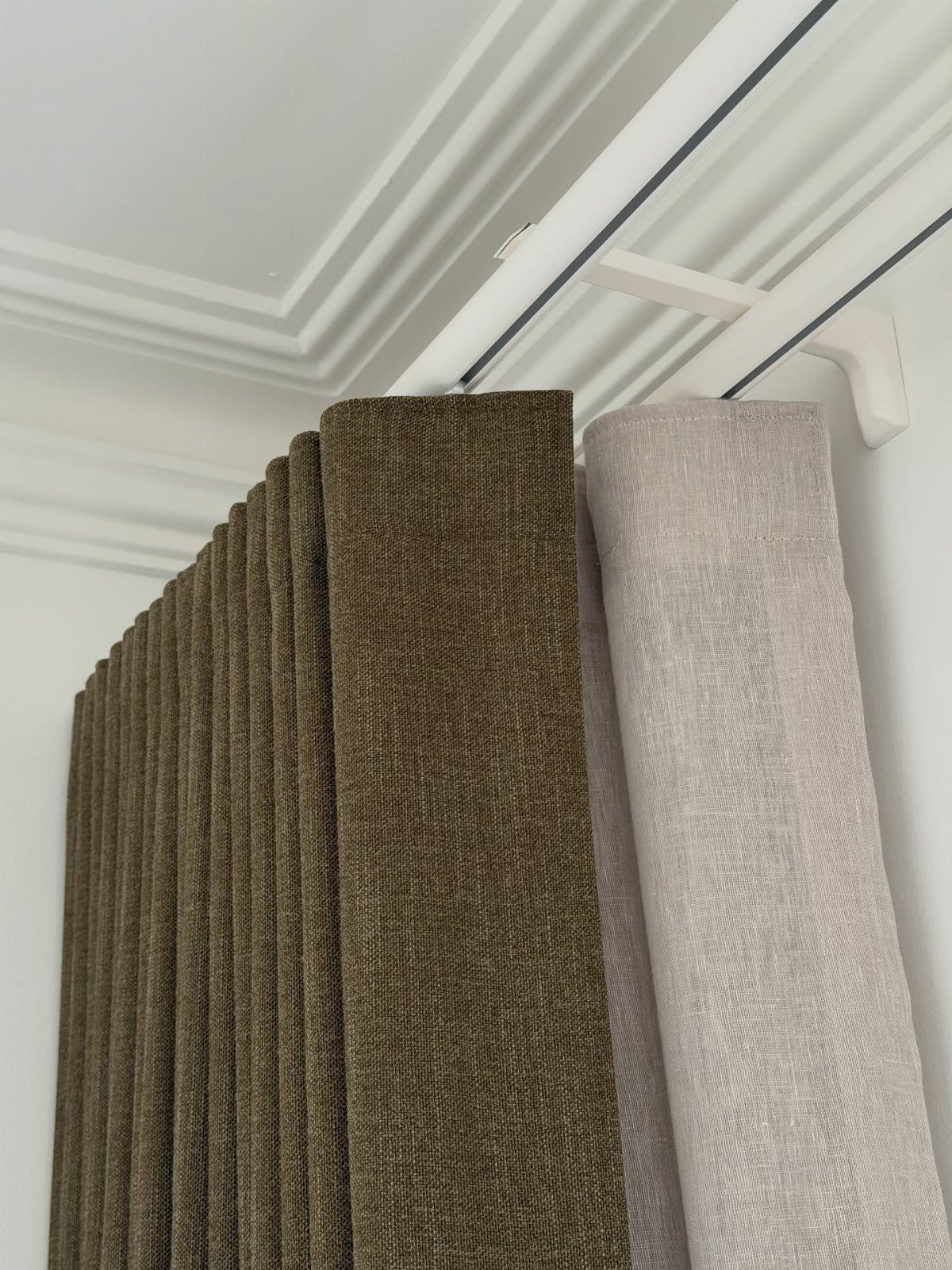 Layered olive green and beige curtains hanging from a white ceiling track.