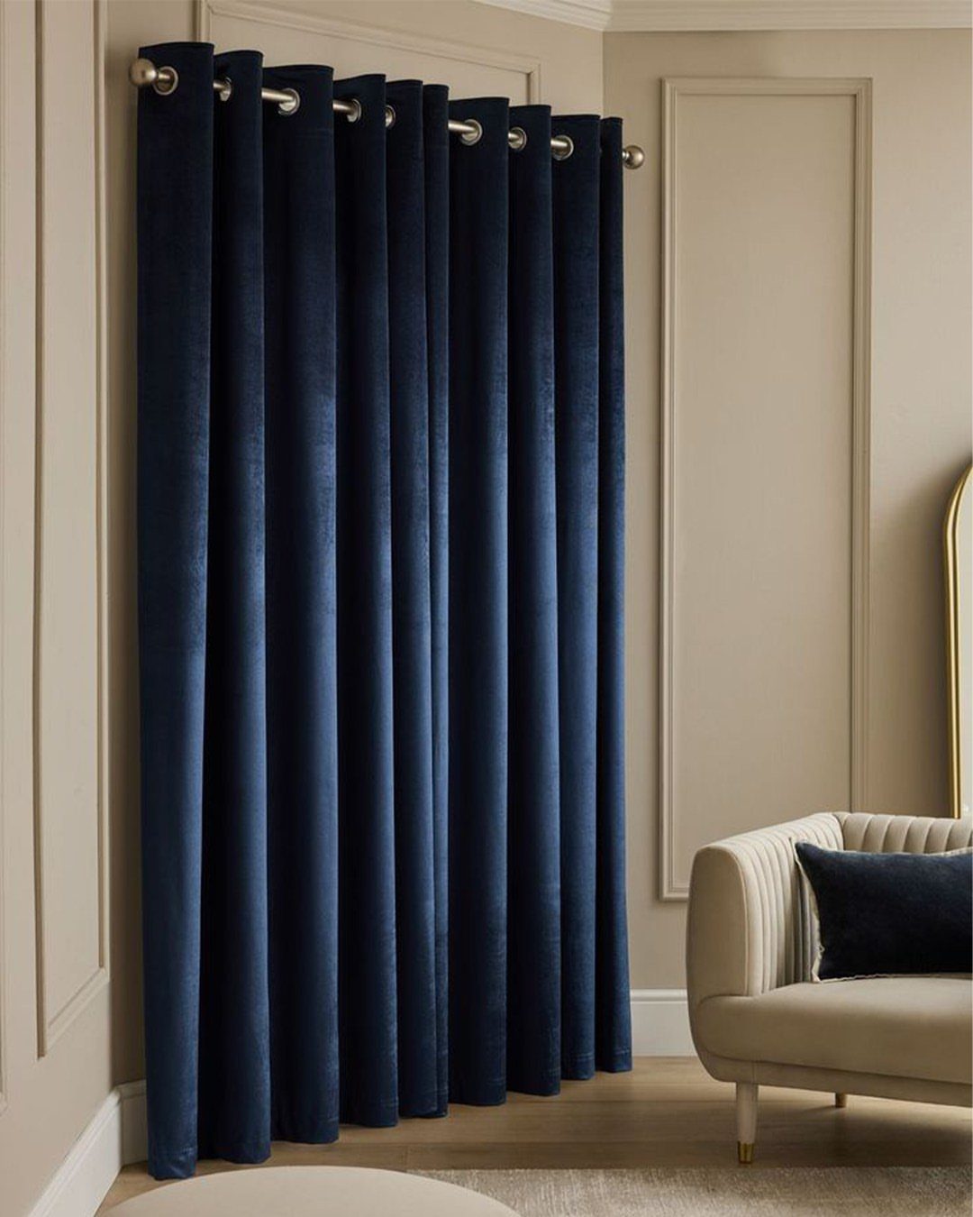 Deep blue velvet curtains hanging in a living room with beige walls.