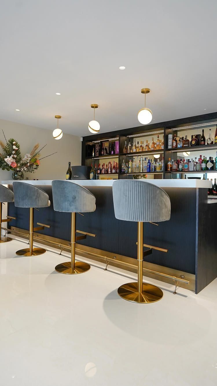 Modern home bar with grey velvet stools and shelves of liquor bottles