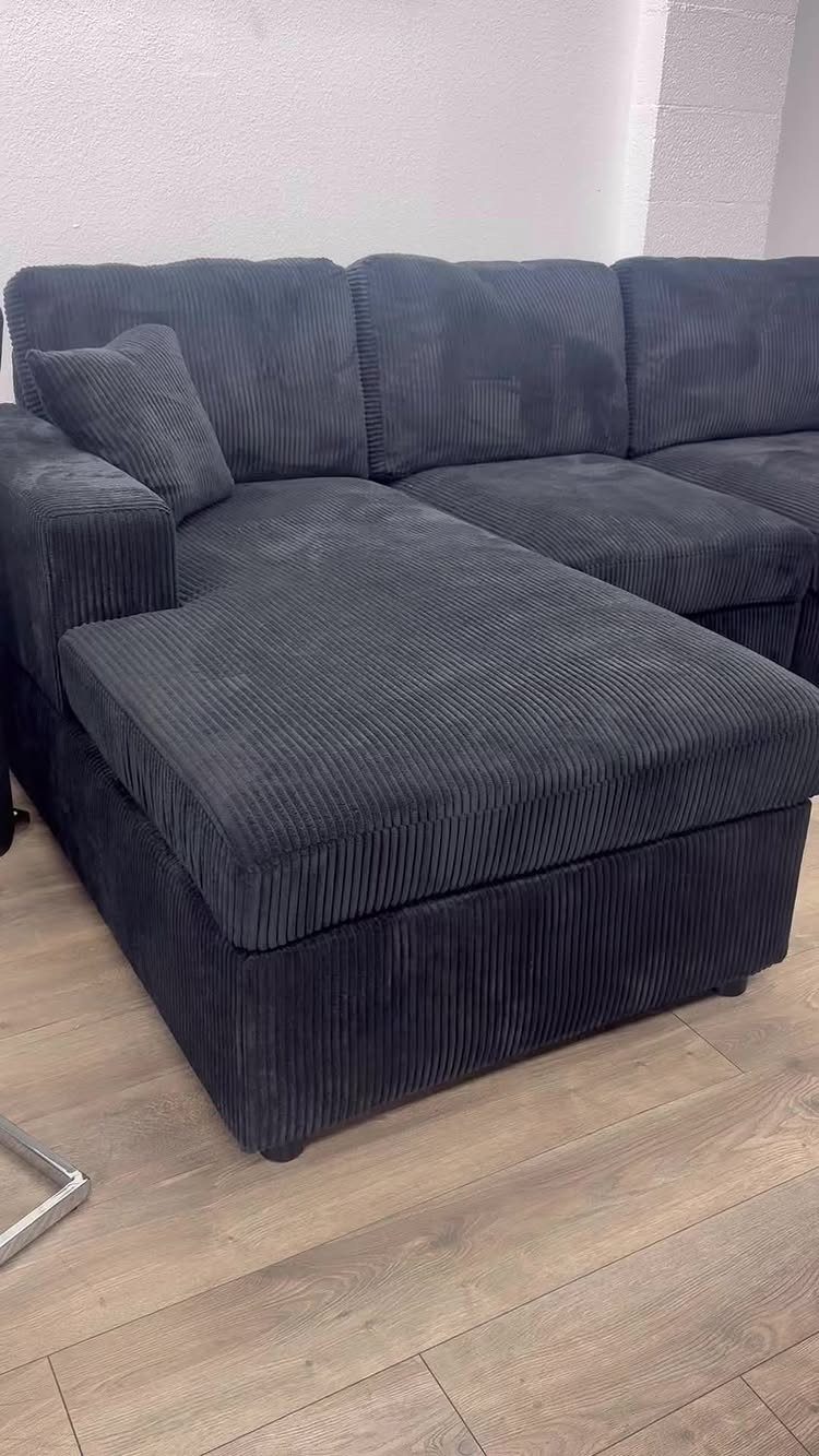 Dark grey corduroy sectional sofa with chaise lounge on light wood flooring.