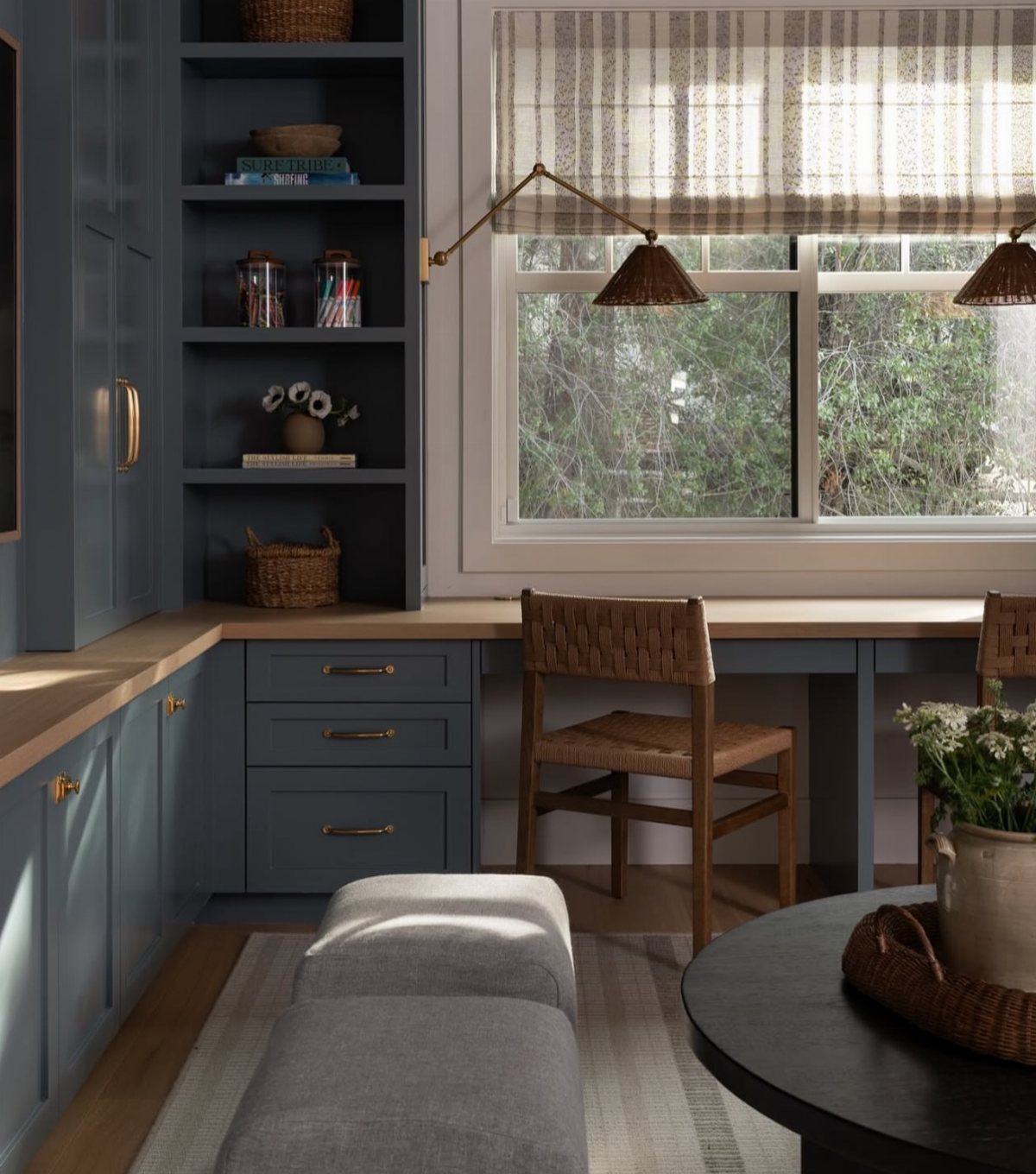 Blue built-in shelving and desk area with a woven chair and grey ottomans.