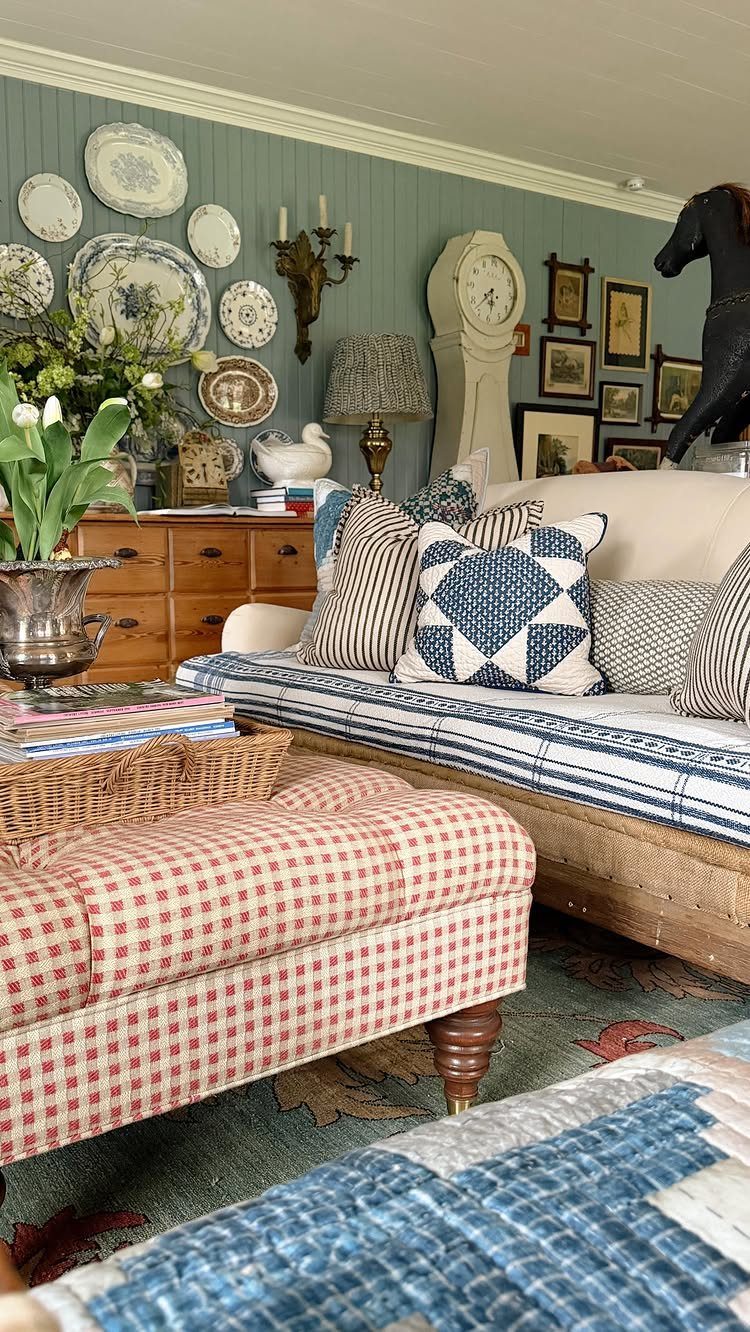 Cozy farmhouse living room with blue paneled walls, gingham ottoman, and patterned cushions.