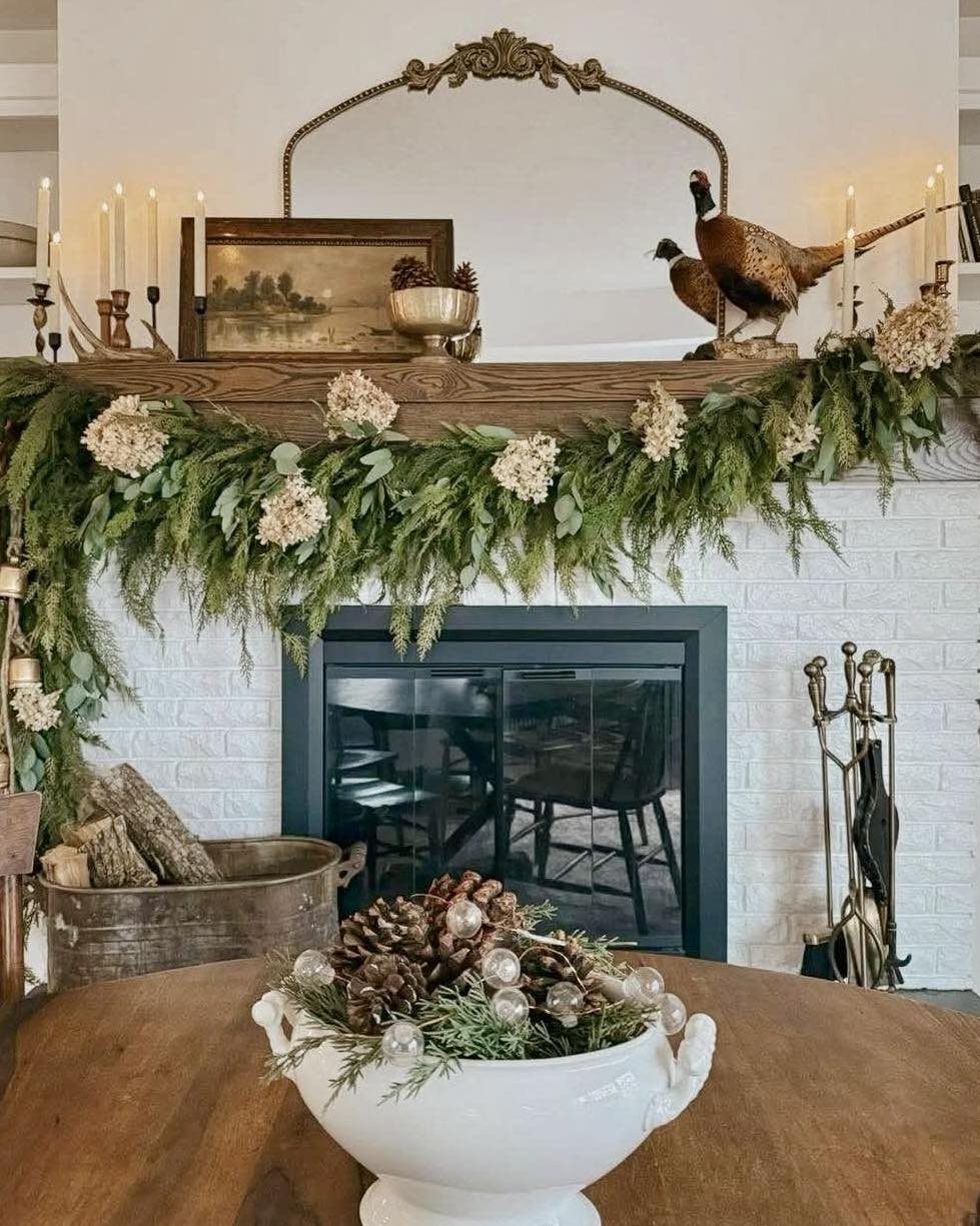 Rustic white brick fireplace with a wooden mantel decorated with greenery and candles.
