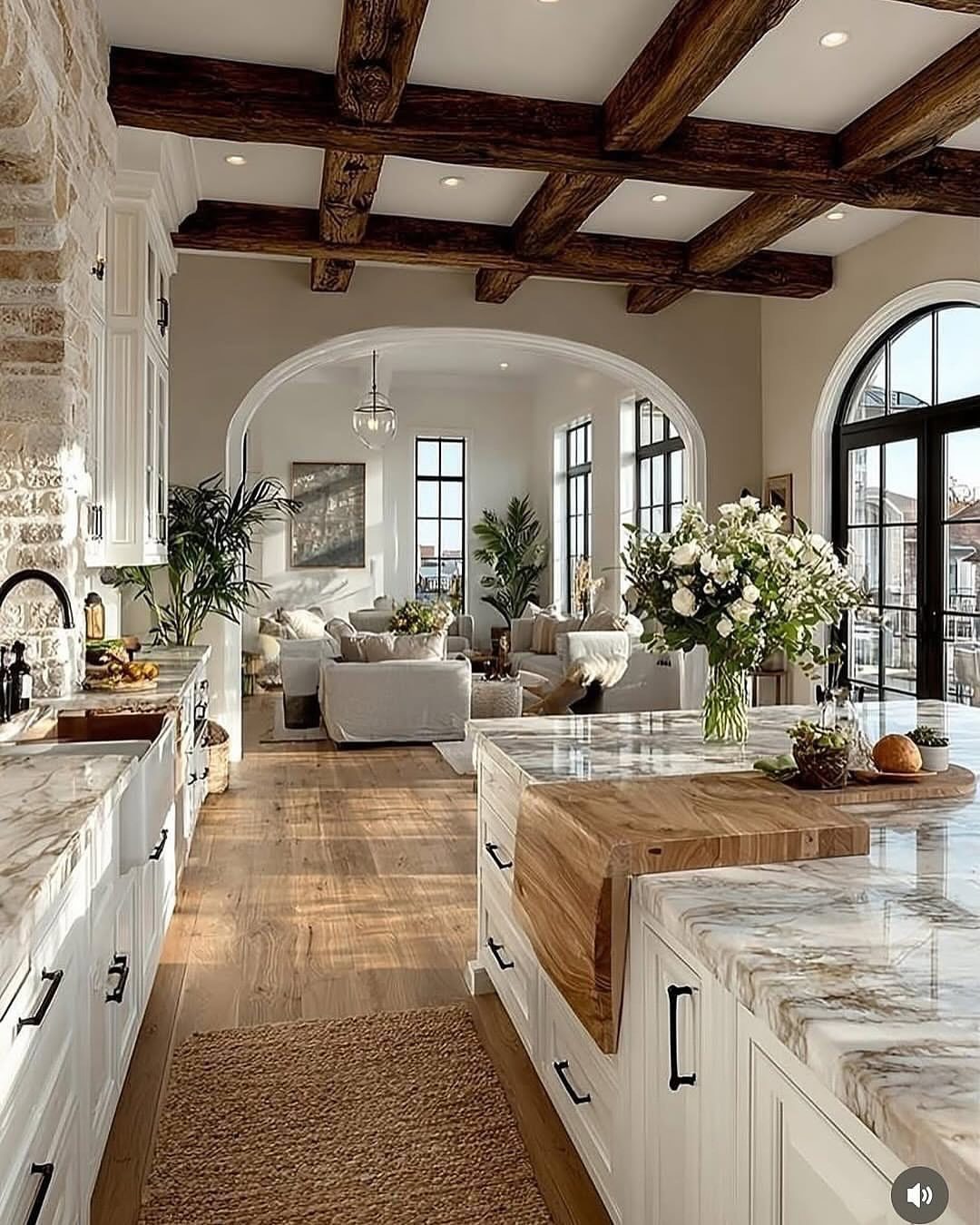 Dark wooden ceiling beams and large arched windows in a bright farmhouse interior.