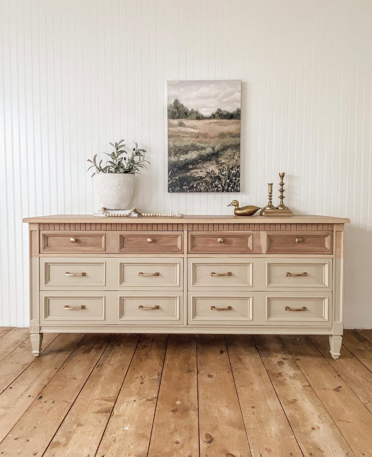 Light-colored wooden dresser with natural wood accents against a white shiplap wall.