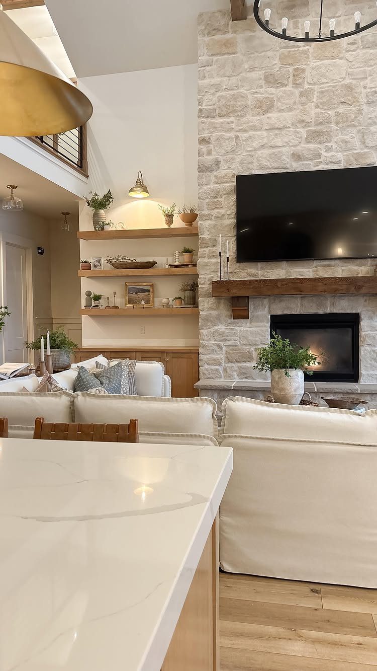 Rustic wooden mantel on a white stone fireplace in a bright farmhouse living room.