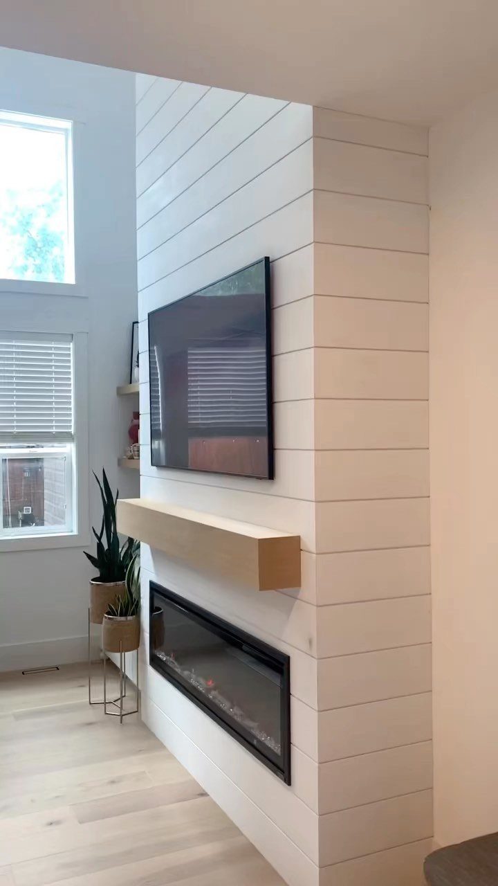 White shiplap wall with a mounted television, wooden mantel, and modern fireplace.