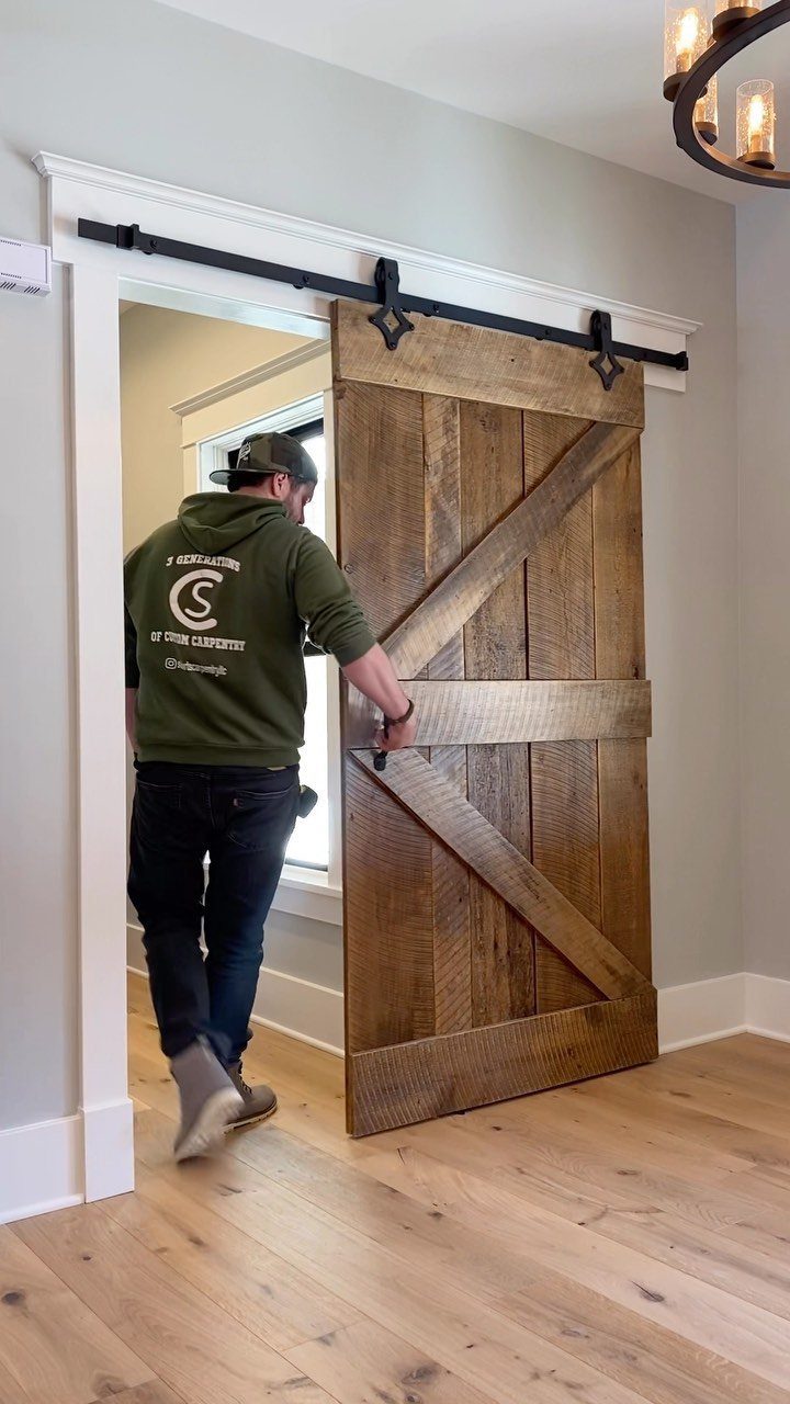 Rustic wooden barn door on a black metal track being slid by a man.
