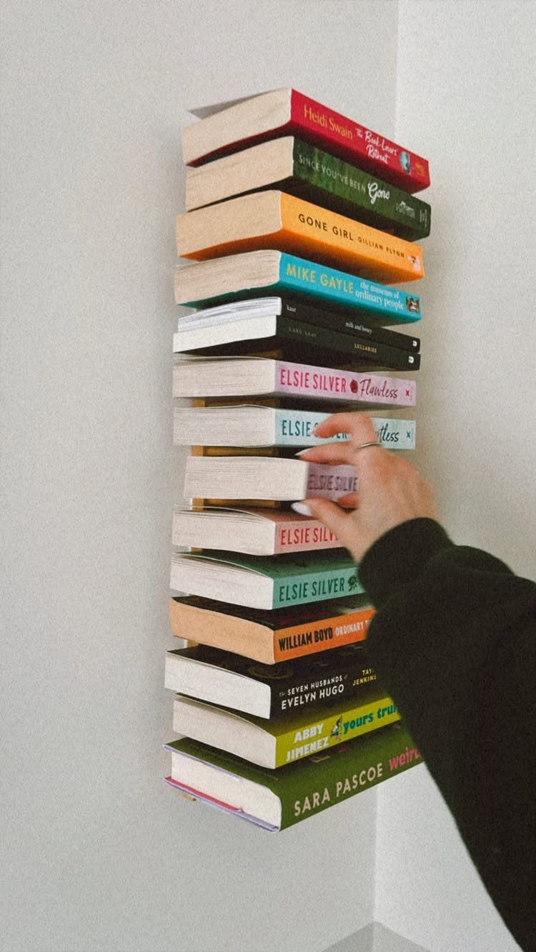 Stacked colorful books appearing to float vertically against a white wall.
