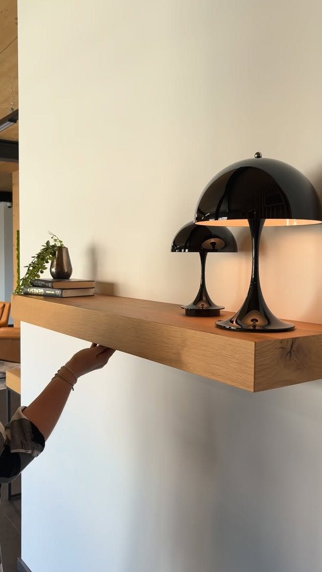 Wooden floating shelf on white wall with black lamps and small plant