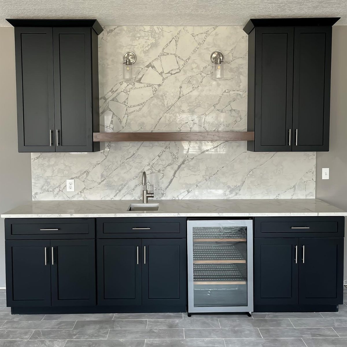 Modern wet bar with navy blue cabinets, marble backsplash, and a wine cooler.