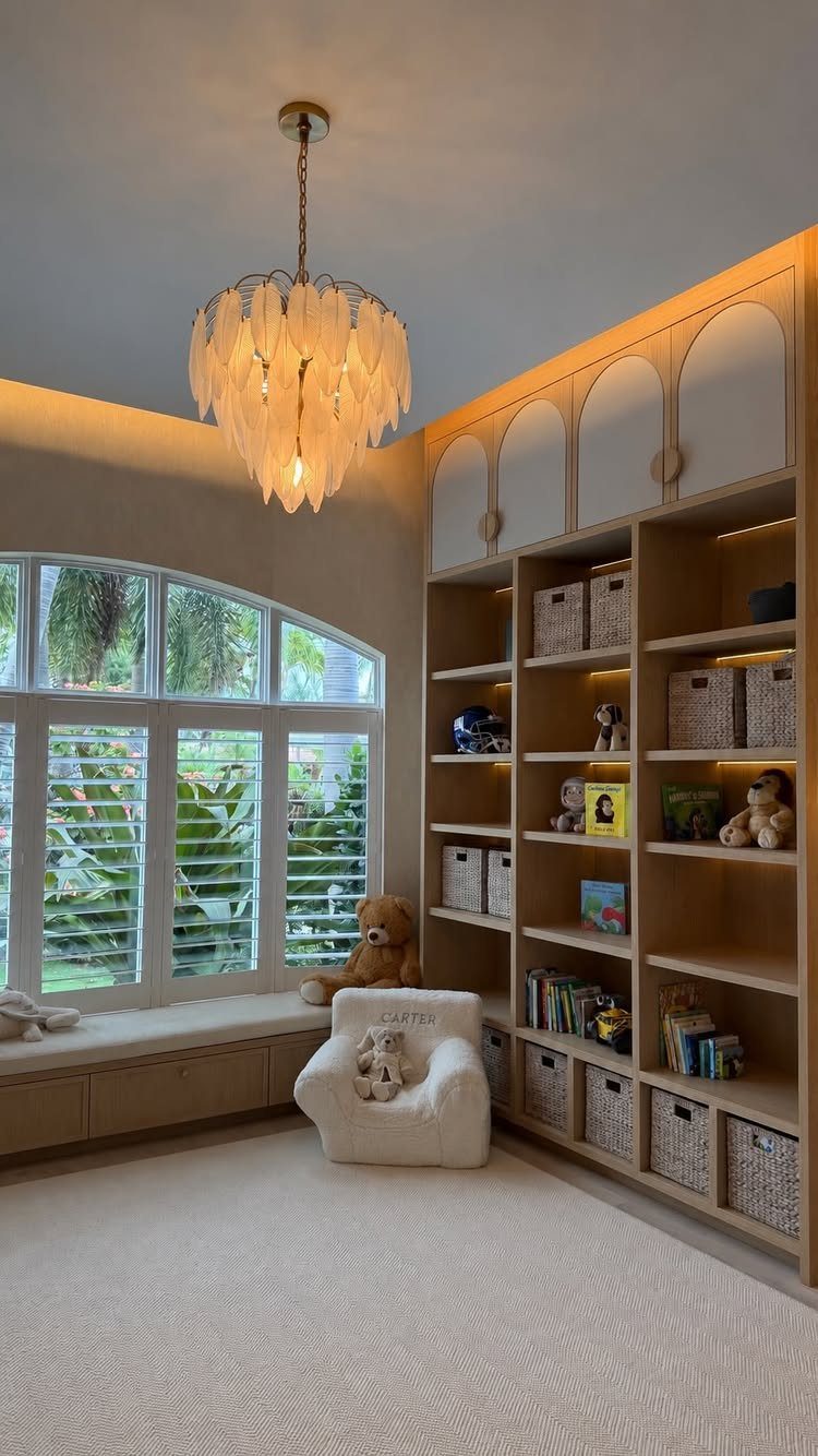 Child's reading nook with a plush white chair, bookshelf, and window seat.