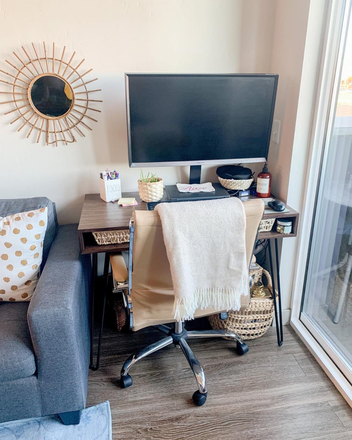 Home office nook with a wooden desk, monitor, and sunburst wall mirror.
