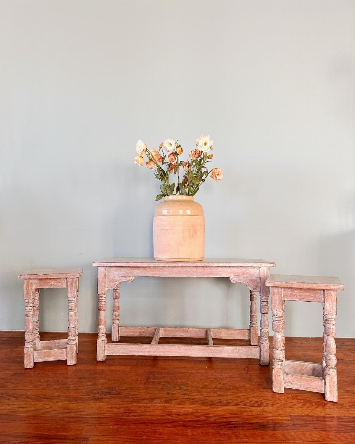 Three rustic light wood tables with a vase of orange flowers on hardwood flooring.