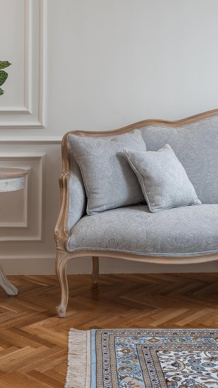 Light grey linen French country sofa with carved wood frame on herringbone floor
