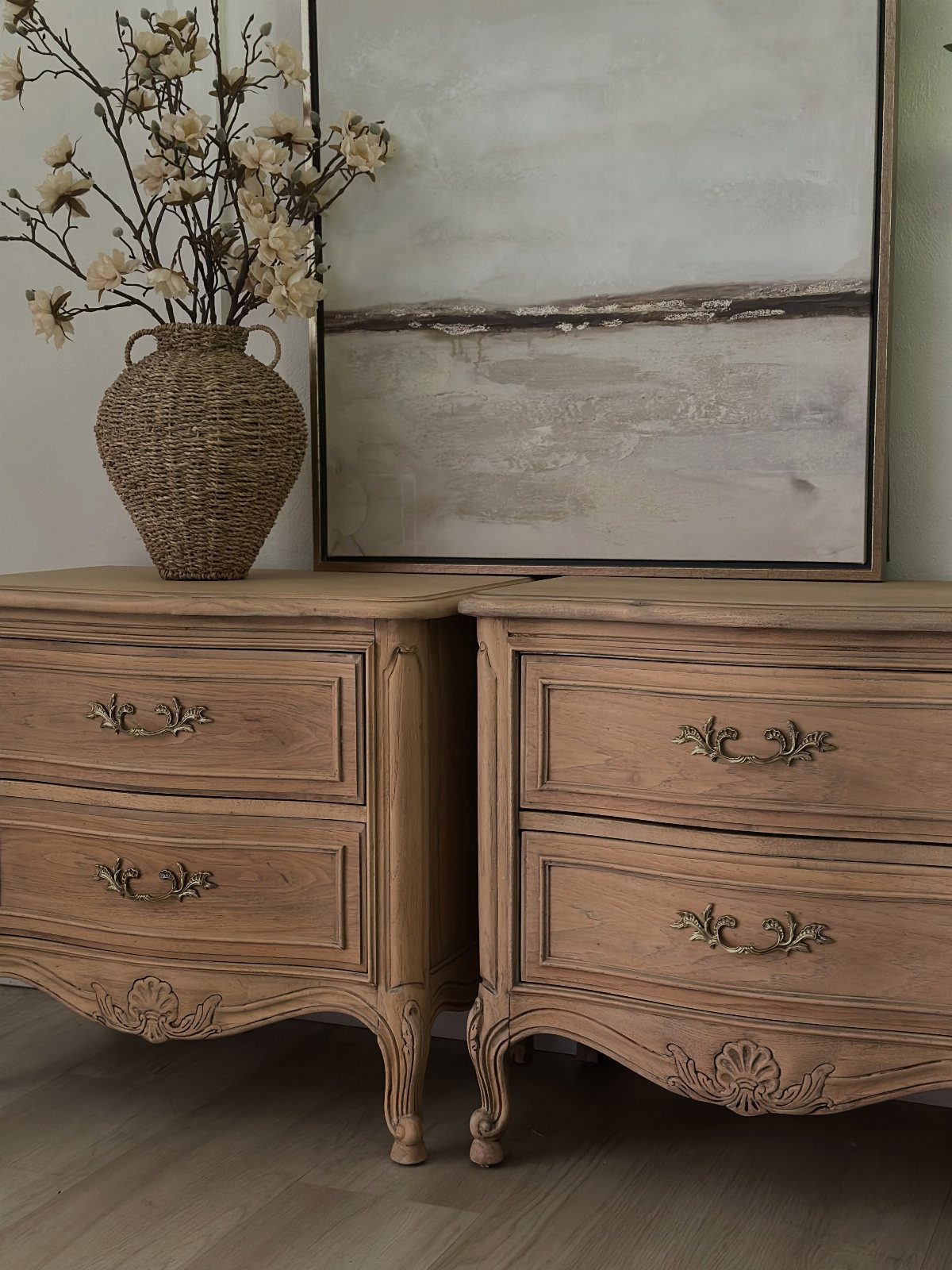 Ornate light wood dressers with gold handles, a woven vase, and abstract art.