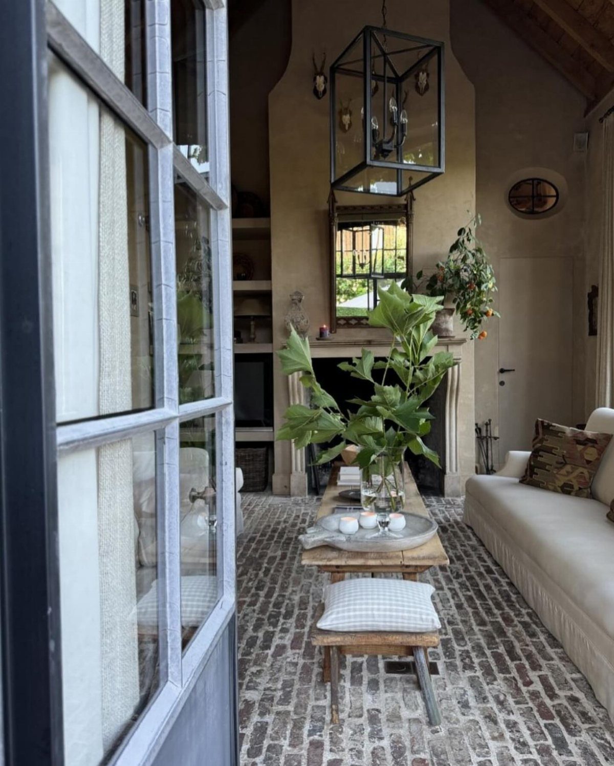 Rustic living room with brick floors, white sofa, and a black lantern chandelier.