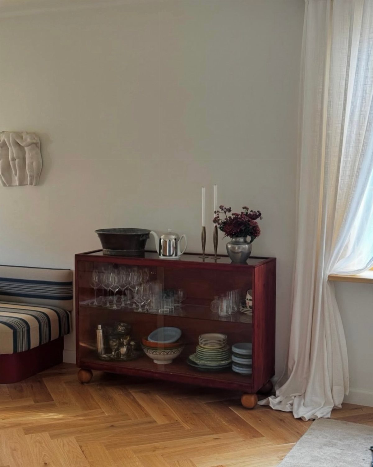 Dark wood sideboard with exposed rounded legs holding glassware against a white wall.