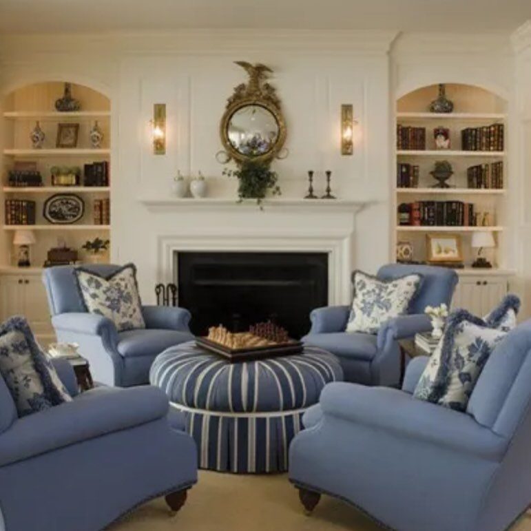Four blue armchairs and a striped ottoman arranged around a white fireplace.