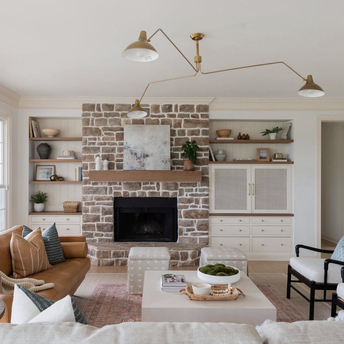 Living room with stone fireplace, brown leather sofa, and white armchair arrangement.
