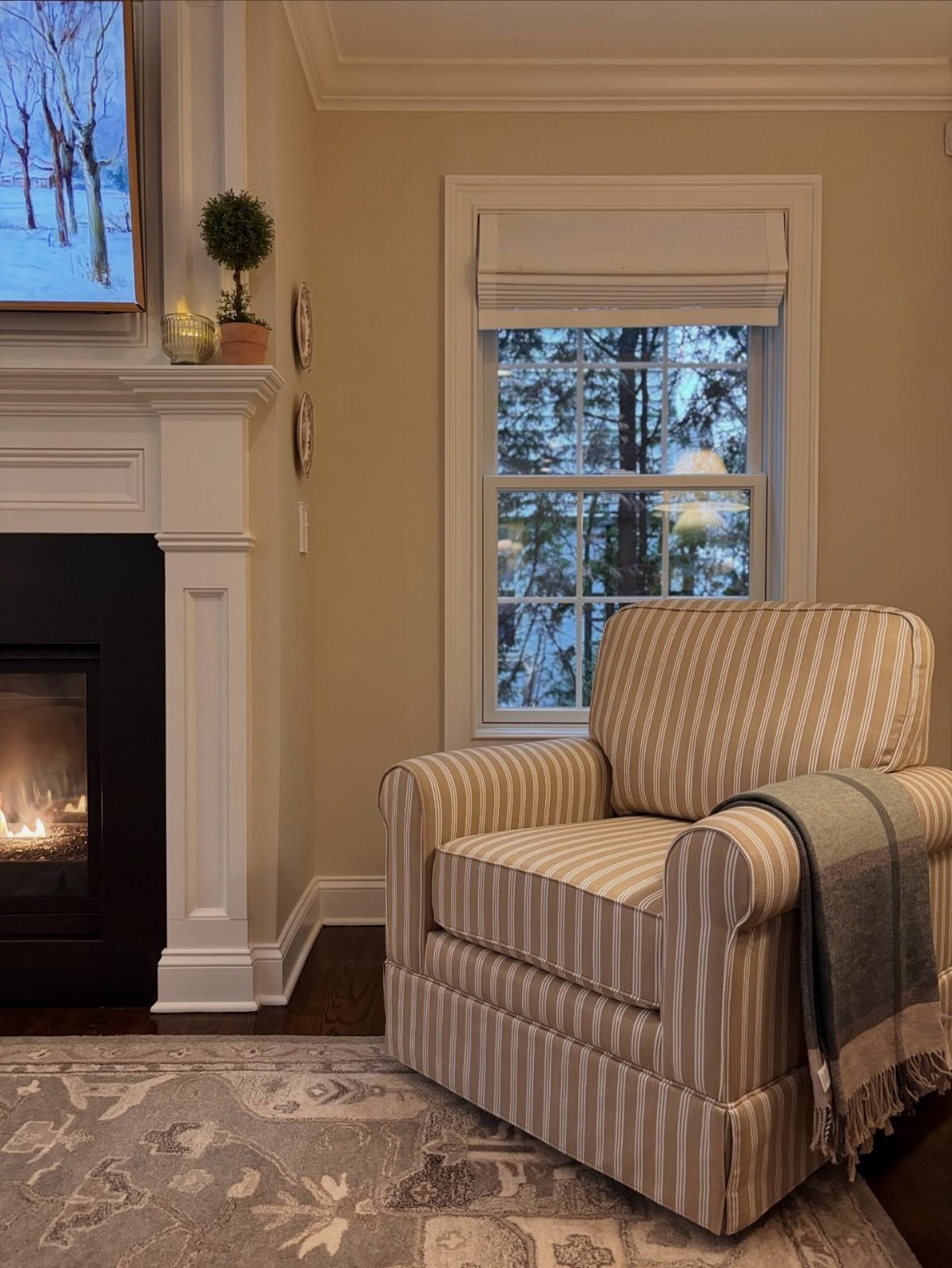 Striped armchair and grey throw blanket positioned next to a white fireplace mantel.