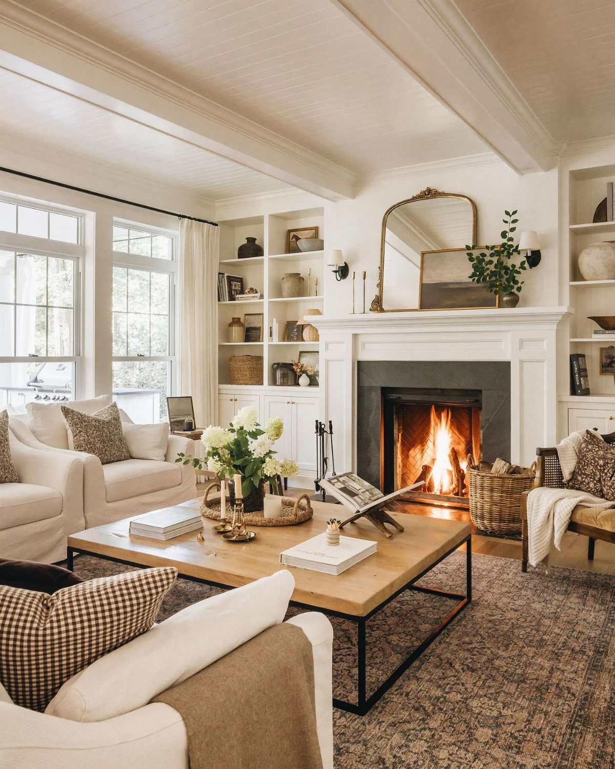 Living room furniture arranged around a white fireplace with a burning fire.
