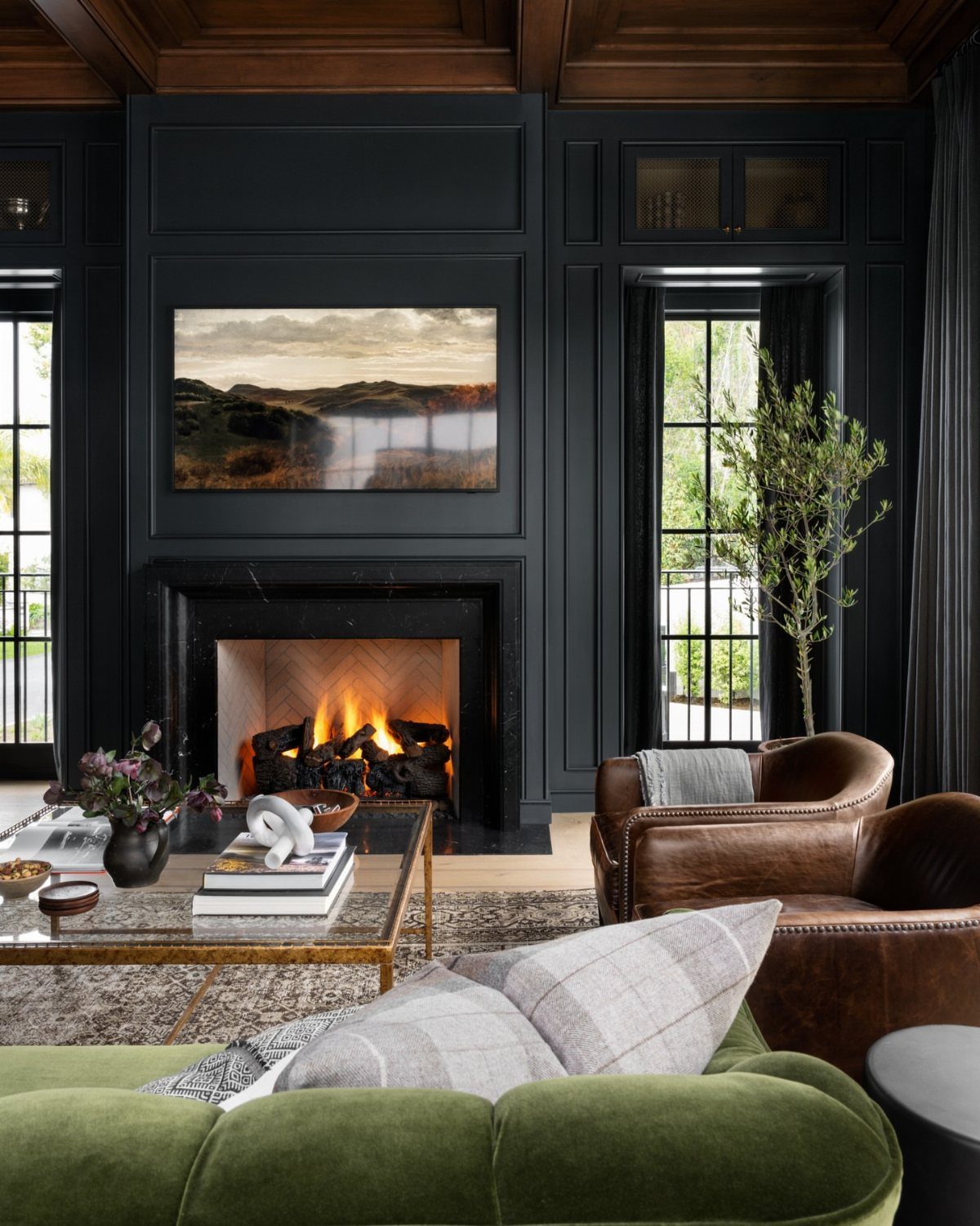 Green velvet sofa facing a lit fireplace in a dark navy living room.