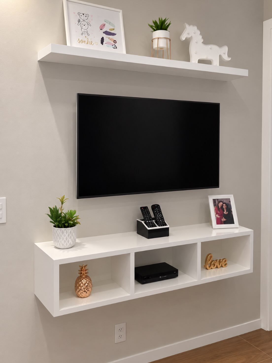 Wall-mounted black TV with a white floating shelf above and low console below.