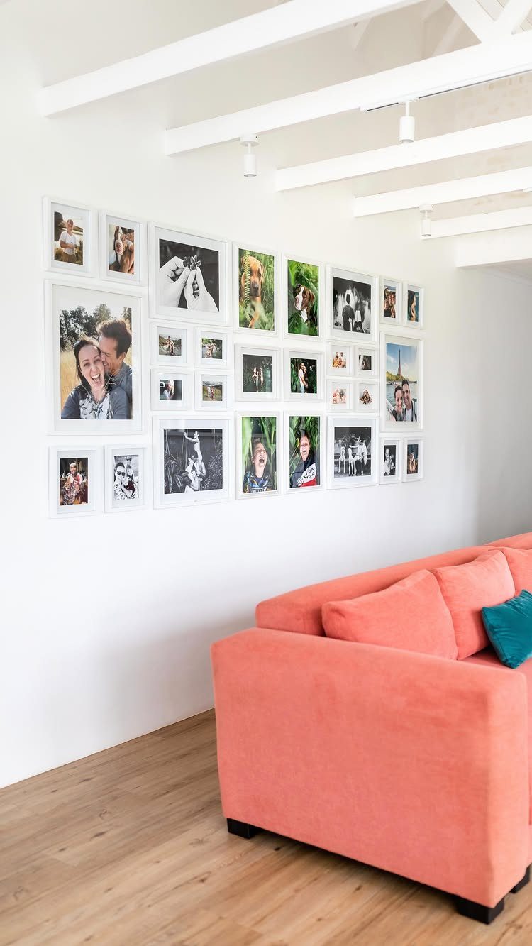 Gallery wall of white-framed photos above a coral sofa in a bright room.