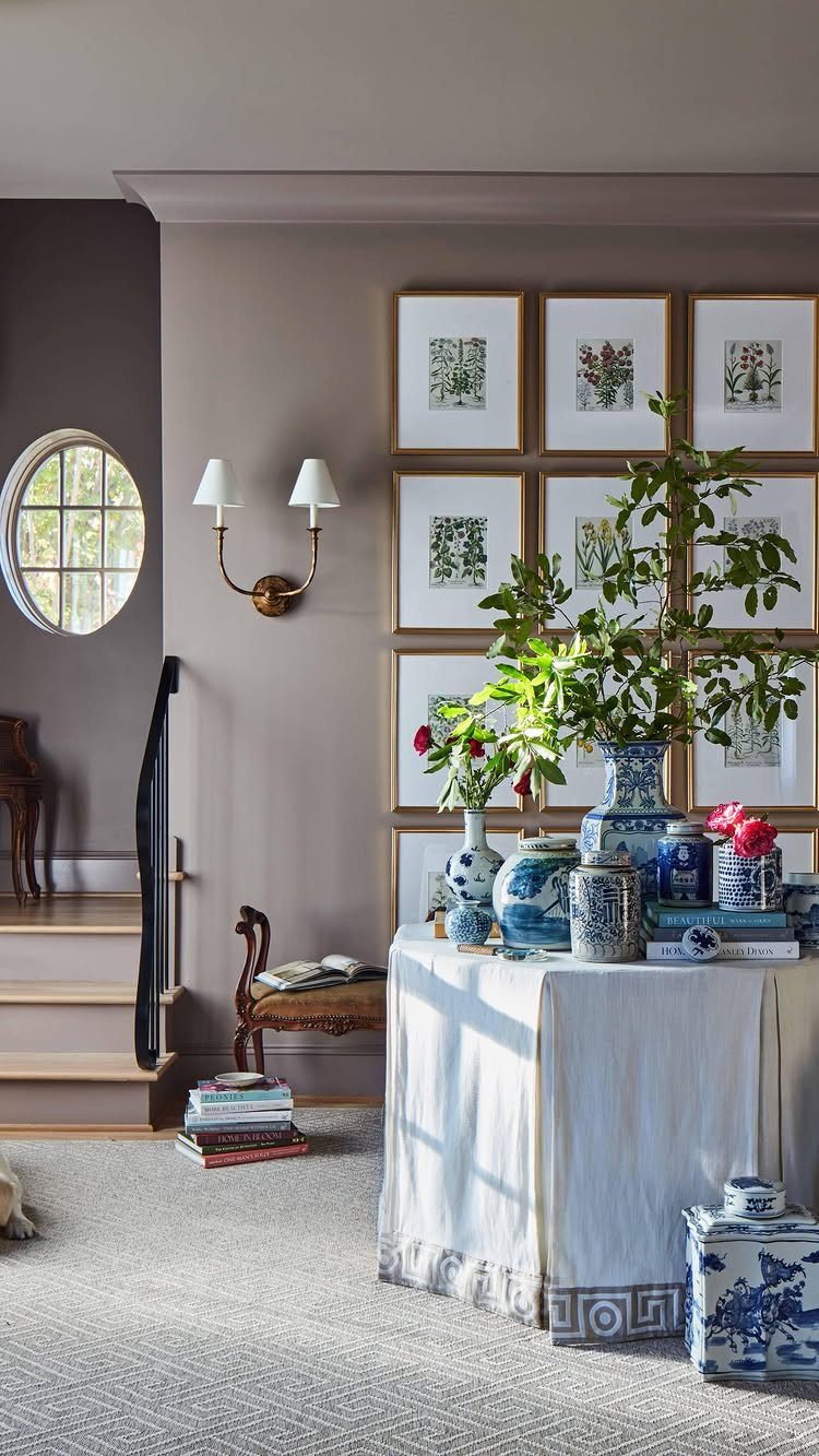 Grid of framed botanical prints on a taupe wall above a decorated table.