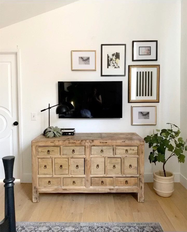 Gallery wall with framed art surrounding a television above a wooden sideboard.