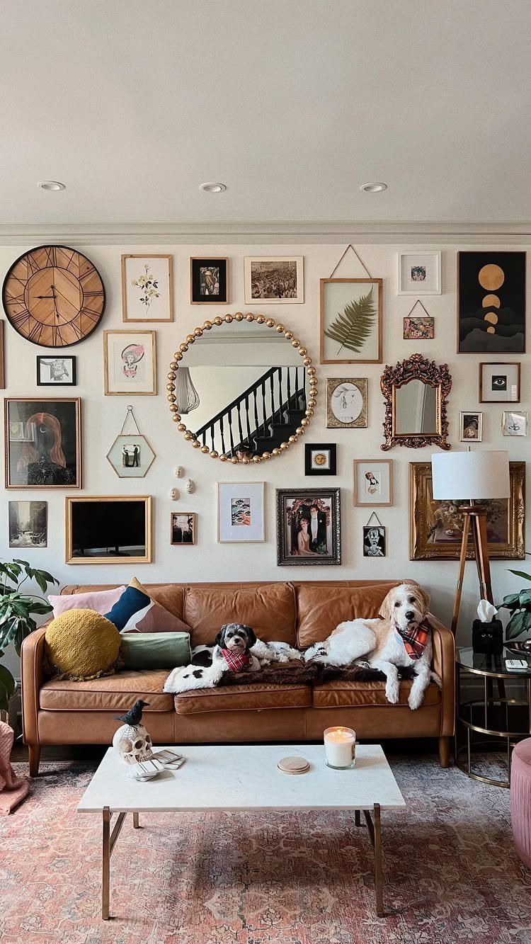 Gallery wall with eclectic frames and mirrors above a brown leather sofa with dogs.
