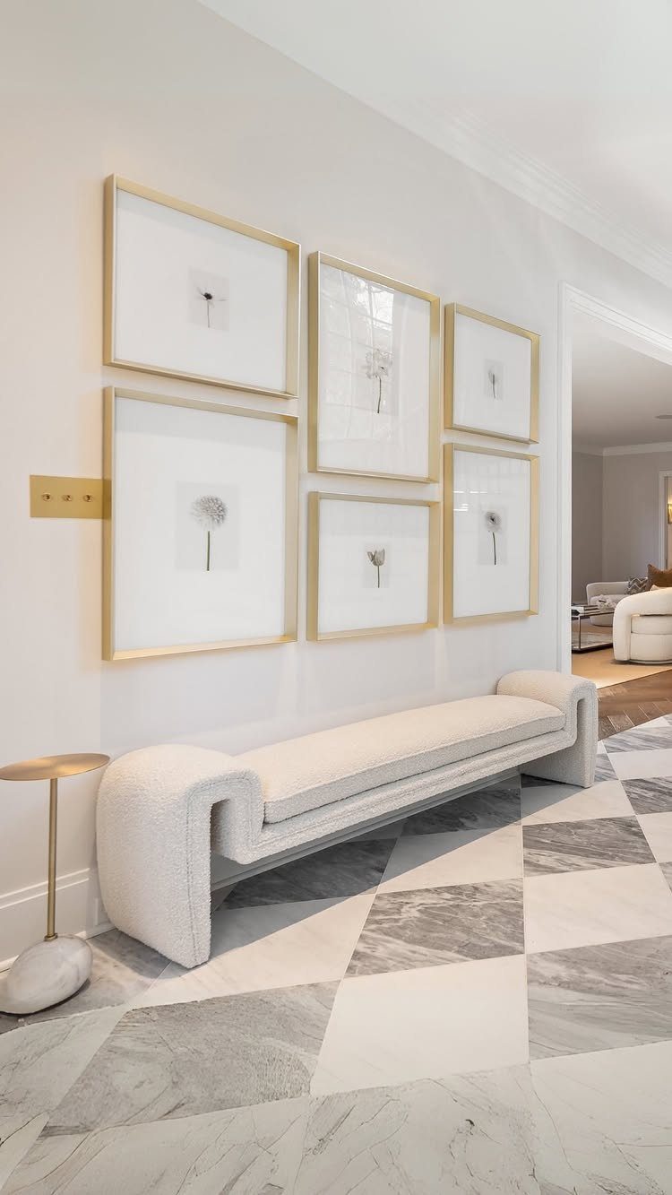 Gold-framed botanical prints arranged with consistent spacing above a white curved bench.