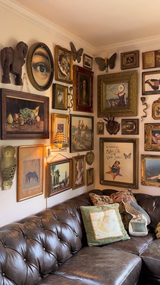 Gallery wall with eclectic framed art and sculptures above a brown leather sofa.