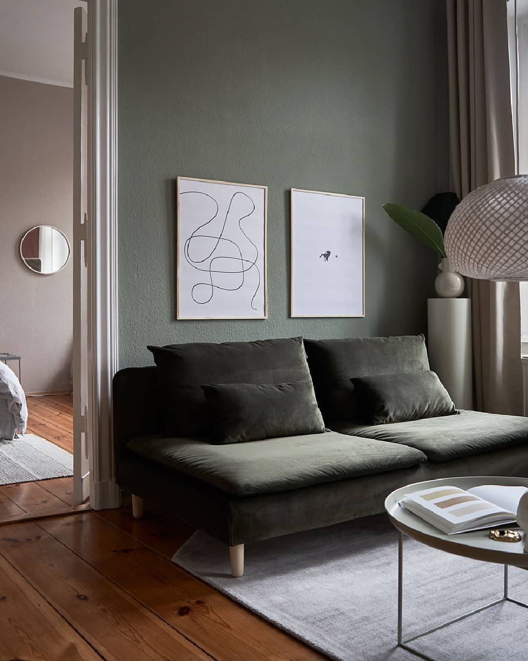 Dark green velvet sofa in a minimalist room with muted green walls and art.