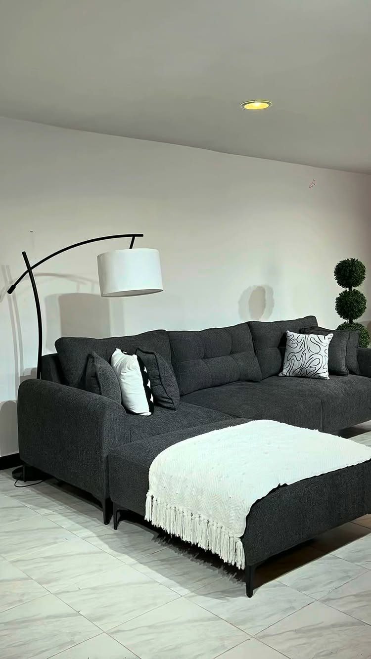 Dark grey sectional sofa with white throw and black arched floor lamp