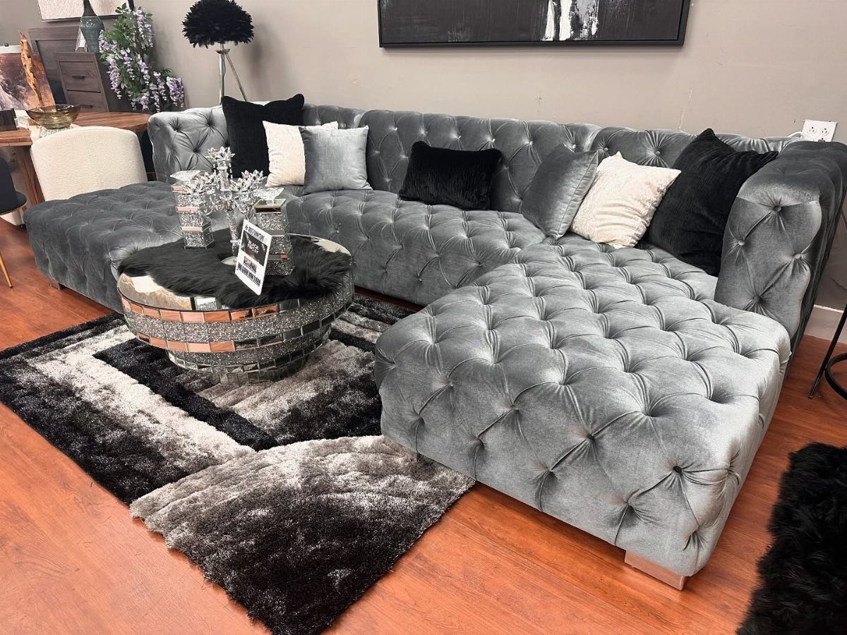 Tufted grey velvet sectional sofa with a mirrored coffee table and shag rug.