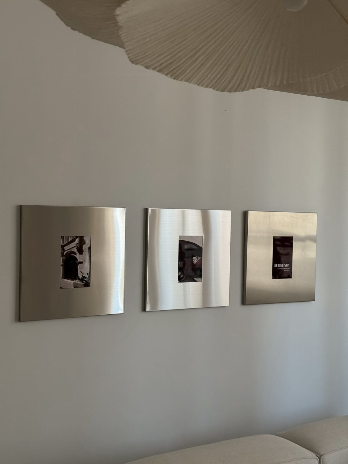 Three square brushed metal art panels hanging on a white wall above a sofa
